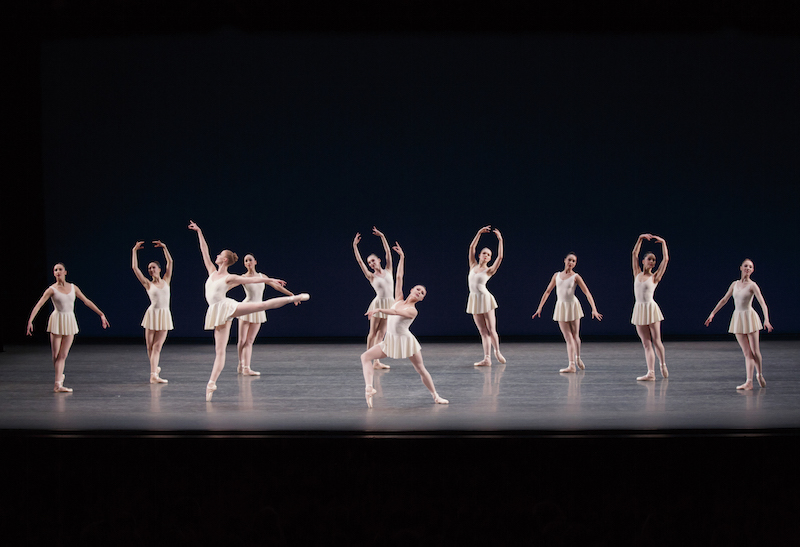 Teresa Reichlen in an arabesque en pointe and Sara Mearns looks out to the audience posing with one of her pointe shoe's tip to the floor, the corp de ballet poses in the background